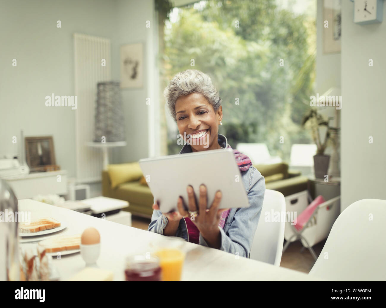 Smiling mature woman using digital tablet at breakfast table Banque D'Images
