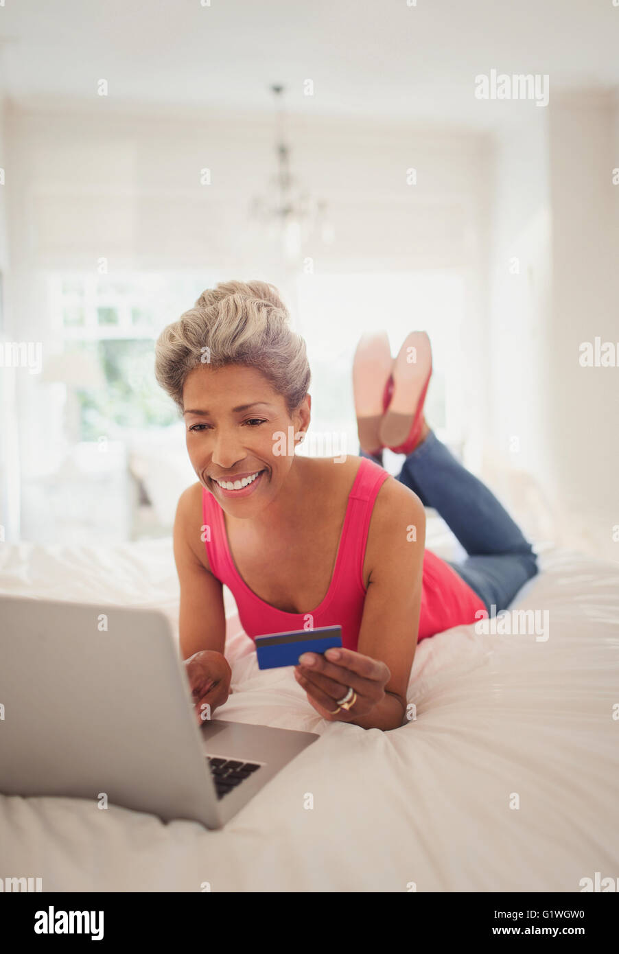 Femme mature avec carte de crédit achats en ligne avec un ordinateur portable sur le lit Banque D'Images