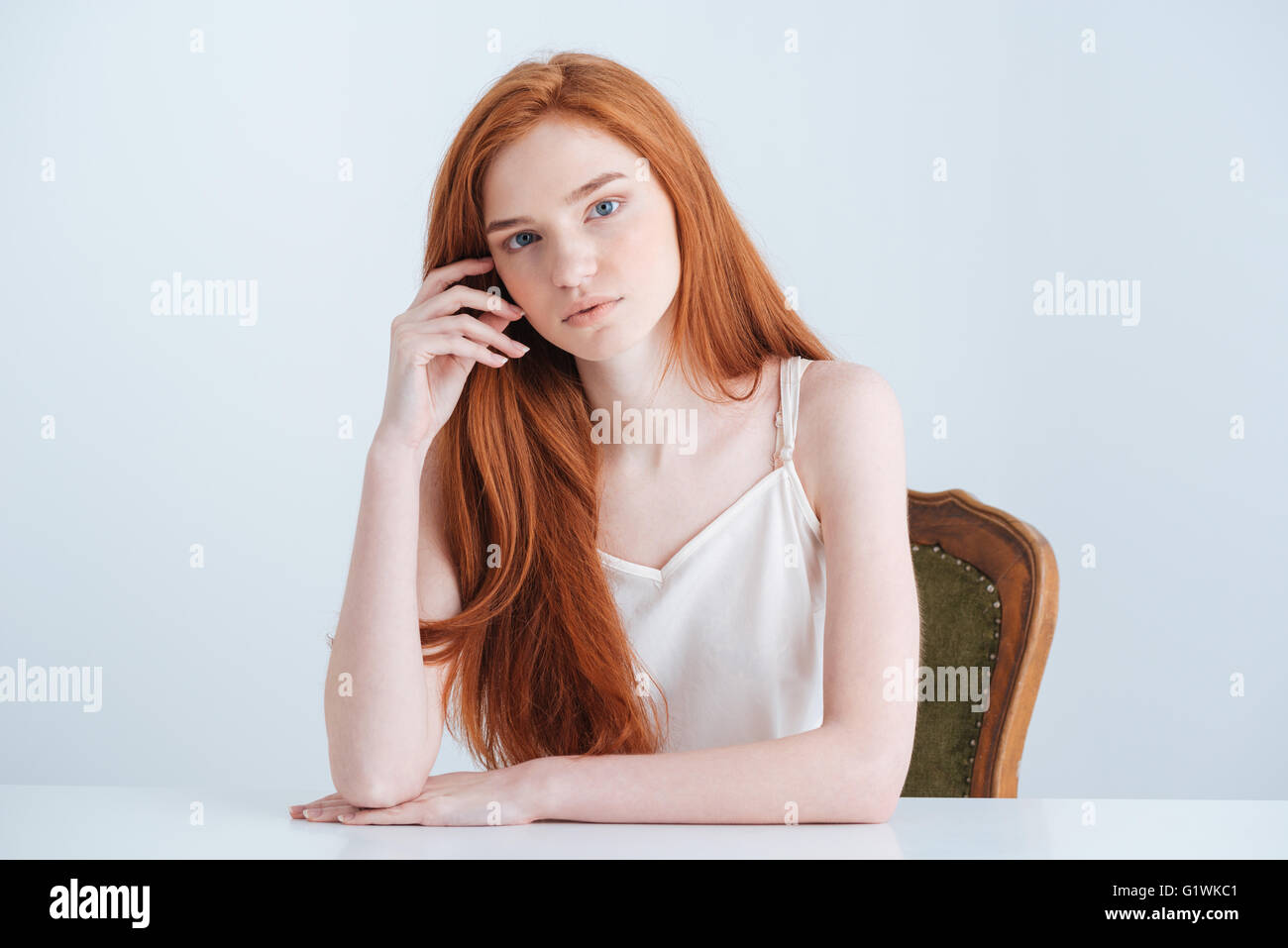 Charmante femme rousse assise à la table et à la caméra à isolé sur fond blanc Banque D'Images