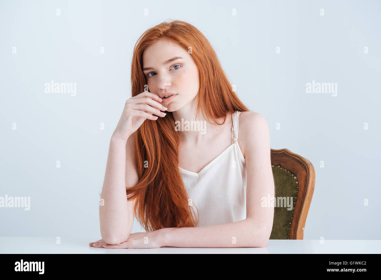 Belle rousse femme assise à la table et à la caméra à isolé sur fond blanc Banque D'Images