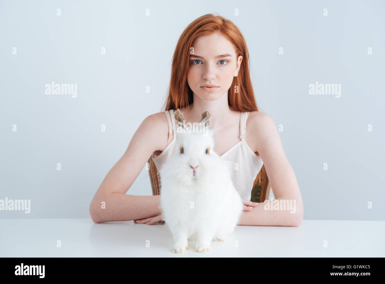 Belle rousse femme assise à la table avec lapin isolé sur fond blanc Banque D'Images