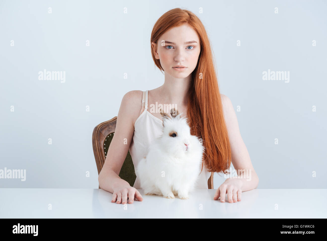 Rousse charmante femme assise à la table avec lapin et looking at camera isolé sur fond blanc Banque D'Images