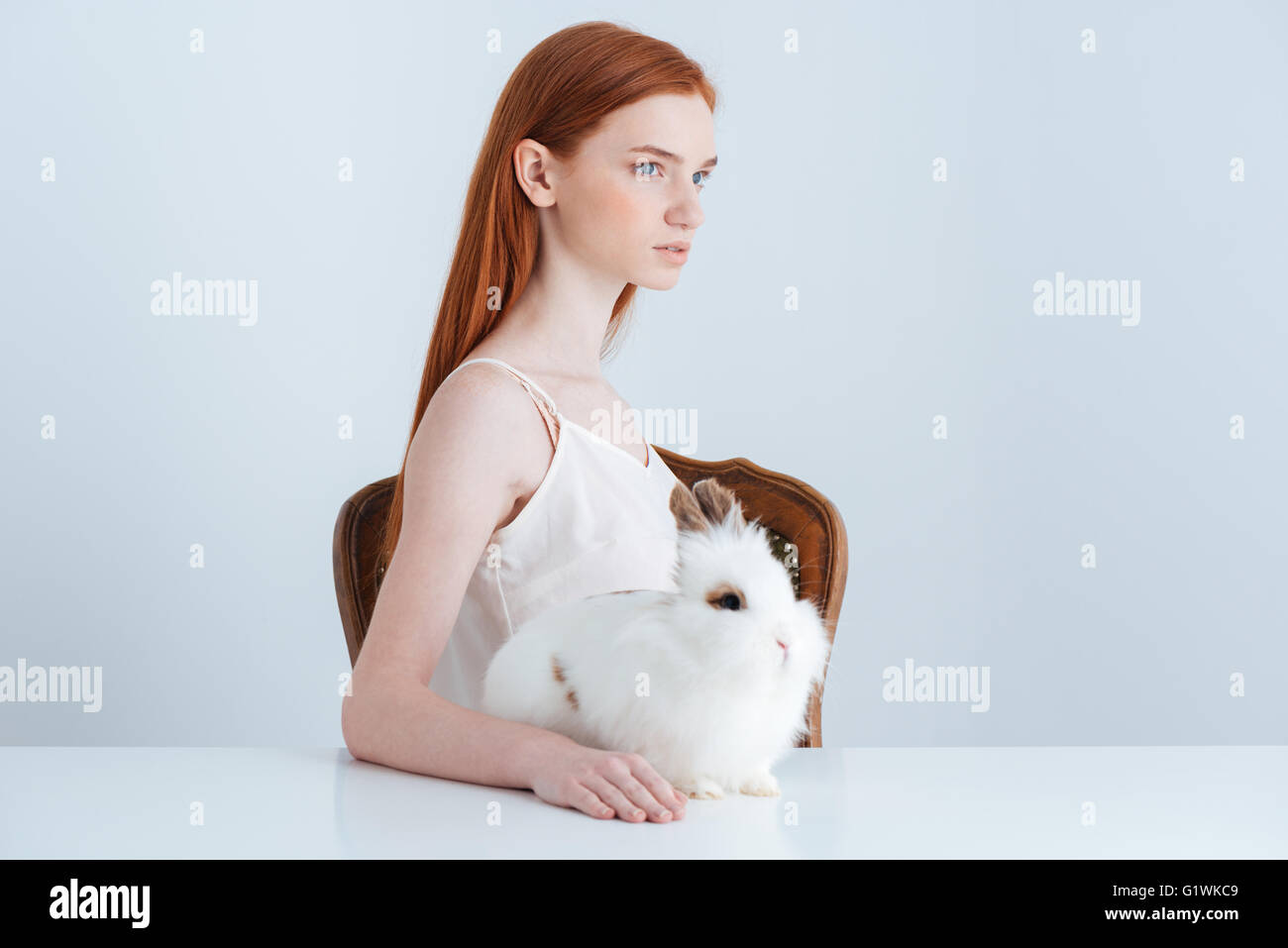 Femme rousse pensif assis à la table avec le lapin et à l'écart isolé sur fond blanc Banque D'Images