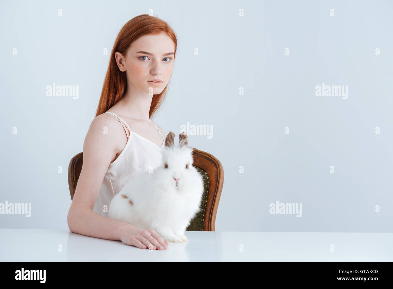 Jeune femme rousse assise à la table avec lapin et looking at camera isolé sur fond blanc Banque D'Images