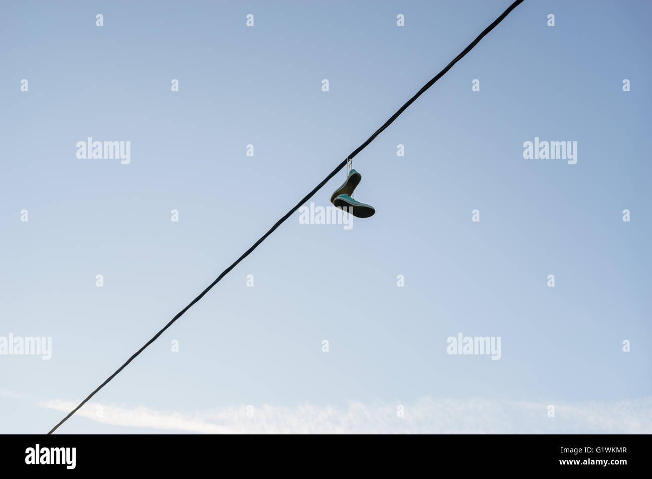 Vieille paire de chaussures se balançant sur la ligne électrique câble contre le ciel bleu, concept de changement de vie Banque D'Images