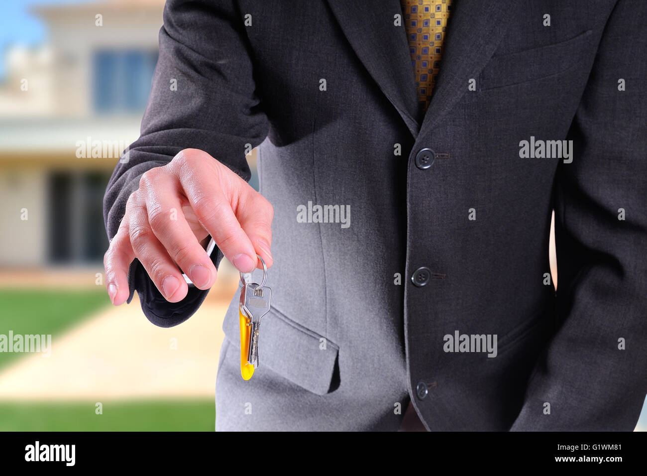 La moitié du corps de l'agent commercial le port d'un costume gris foncé remise des clés pour l'achat d'une maison avec home background Banque D'Images