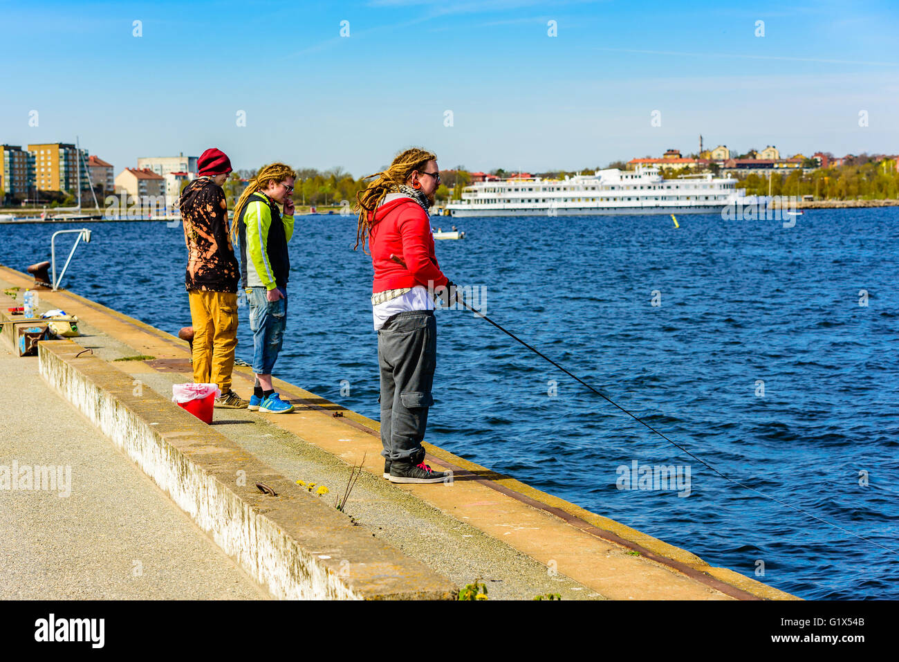 Karlskrona, Suède - mai 3, 2016 : Trois jeunes adultes à quai permanent. L'une est la pêche après le hareng. Deux dreadlocks ont une ha Banque D'Images