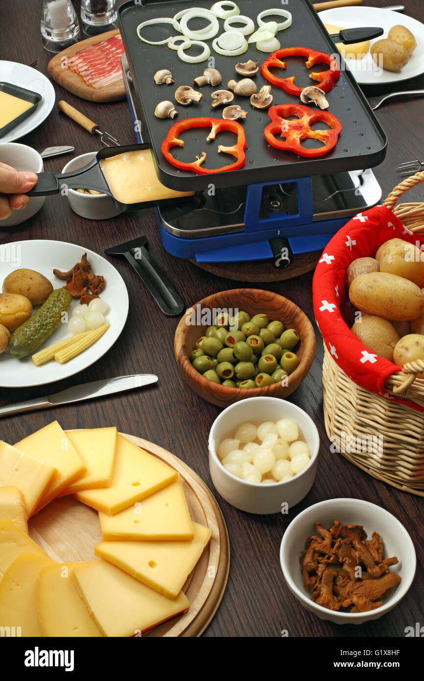 Photo d'un tableau plein d'éléments pour un dîner Raclette traditionnel, y compris les tranches de fromage, oignons blancs, pommes de terre, olives, mu Banque D'Images