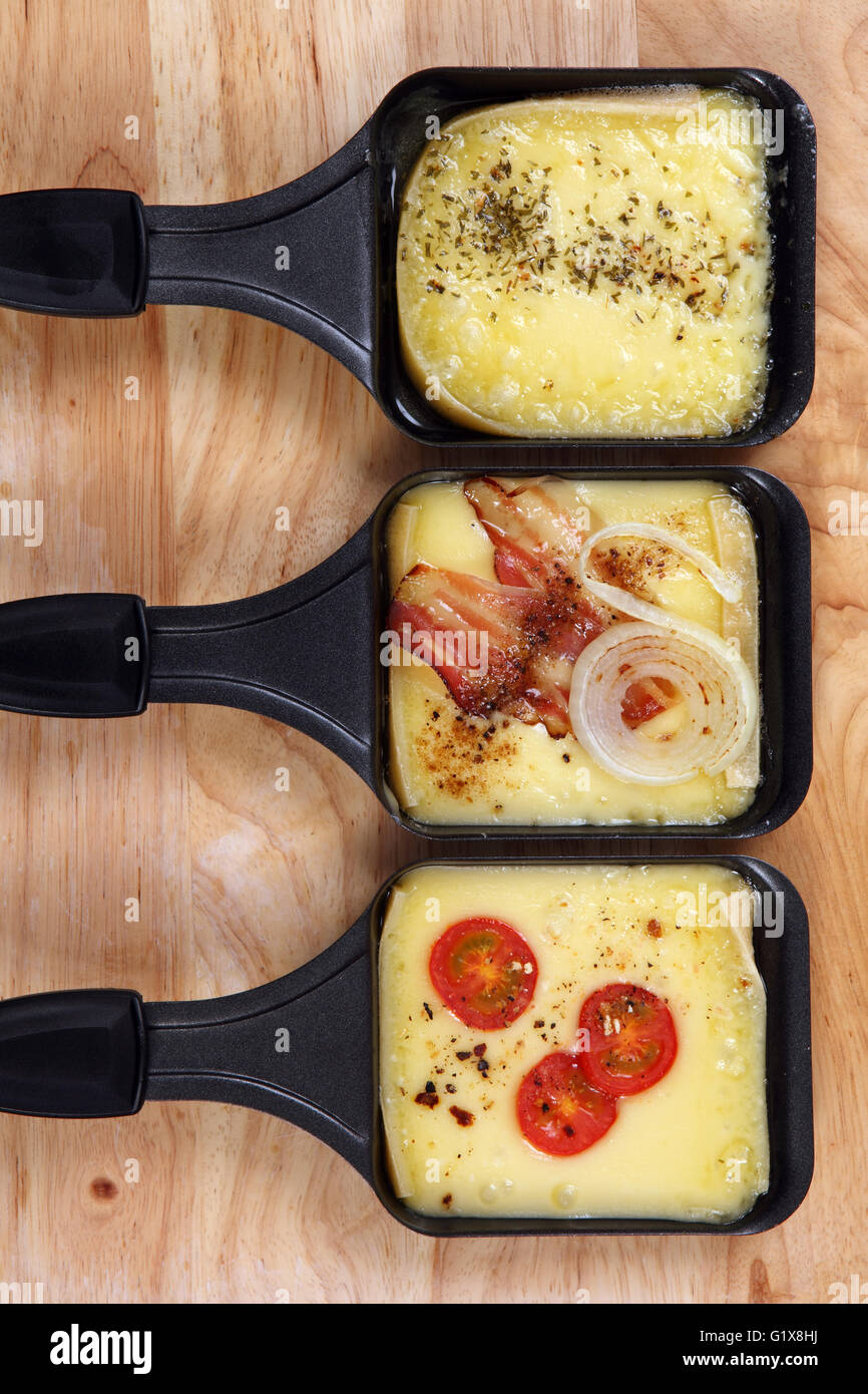 Photo d'une raclette avec trois plateaux de fromage fondu, de fines herbes, tomate cerise, bacon et l'oignon. Banque D'Images