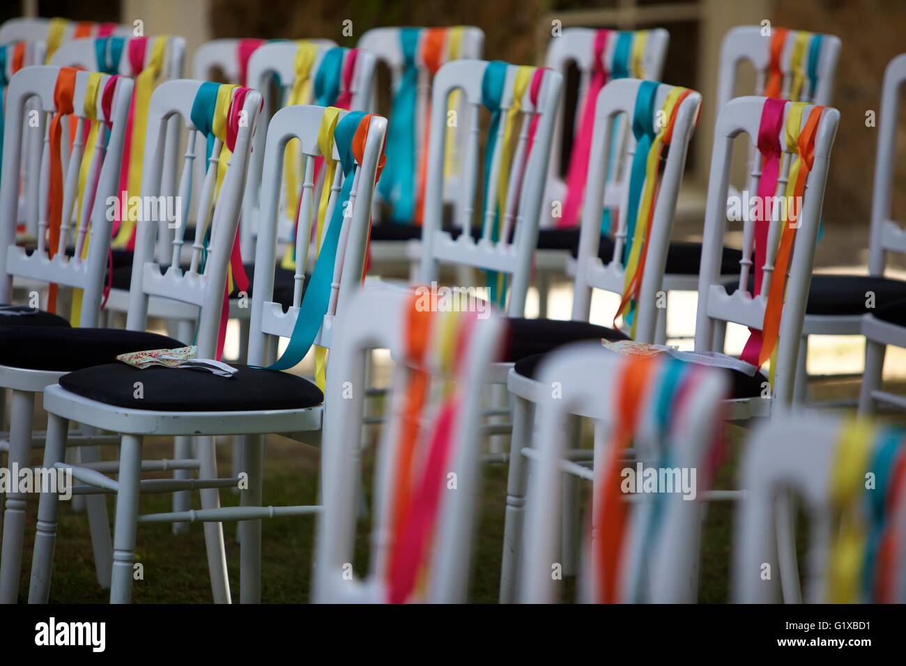 Rangée de chaises blanches couvertes de rubans colorés en préparation pour un mariage. Banque D'Images Rangée de chaises blanches couvertes de rubans colorés en préparation pour un mariage. Banque D'Images