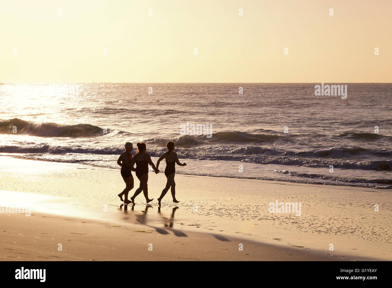 Trois femmes s'exécutant sur la plage dans l'eau avec rétroéclairage, Caloundra, Queensland, Australie Banque D'Images
