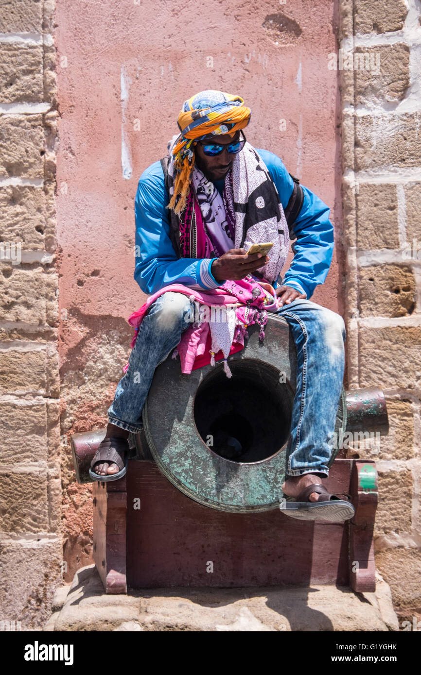 Habillés de couleurs vives à l'écran de l'homme au téléphone tandis qu'assis sur un vieux canon à Essaouira,Maroc Banque D'Images