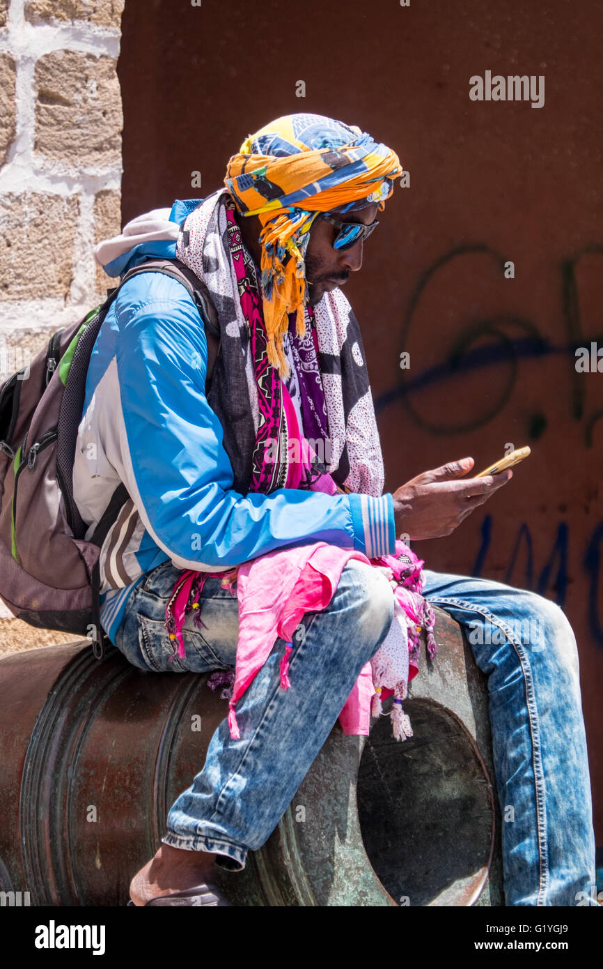 Habillés de couleurs vives à l'écran de l'homme au téléphone tandis qu'assis sur un vieux canon à Essaouira,Maroc Banque D'Images