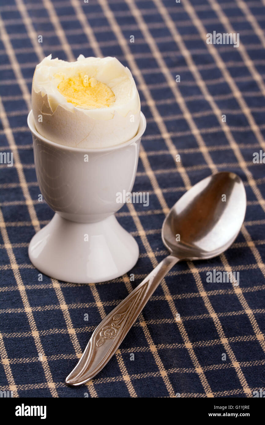 Egg cup avec un oeuf sur le dessus d'une nappe bleu foncé, avec cuillère Banque D'Images