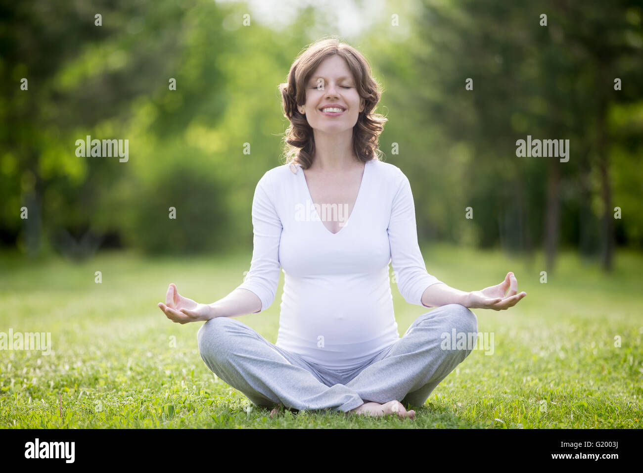 Portrait de jeunes femmes enceintes de travail modèle de parc. Avenir souriant attend maman enfant assis en tailleur et de méditer Banque D'Images