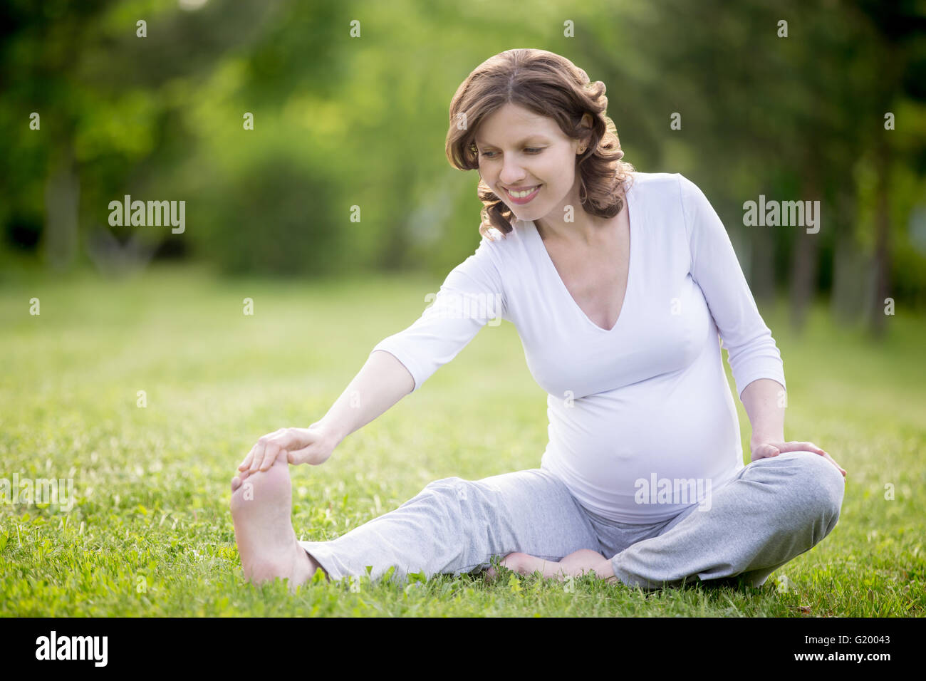 Portrait de jeunes femmes enceintes de travail modèle de parc. Avenir souriant maman faisant des exercices d'étirement à l'extérieur. Tendon assis Banque D'Images