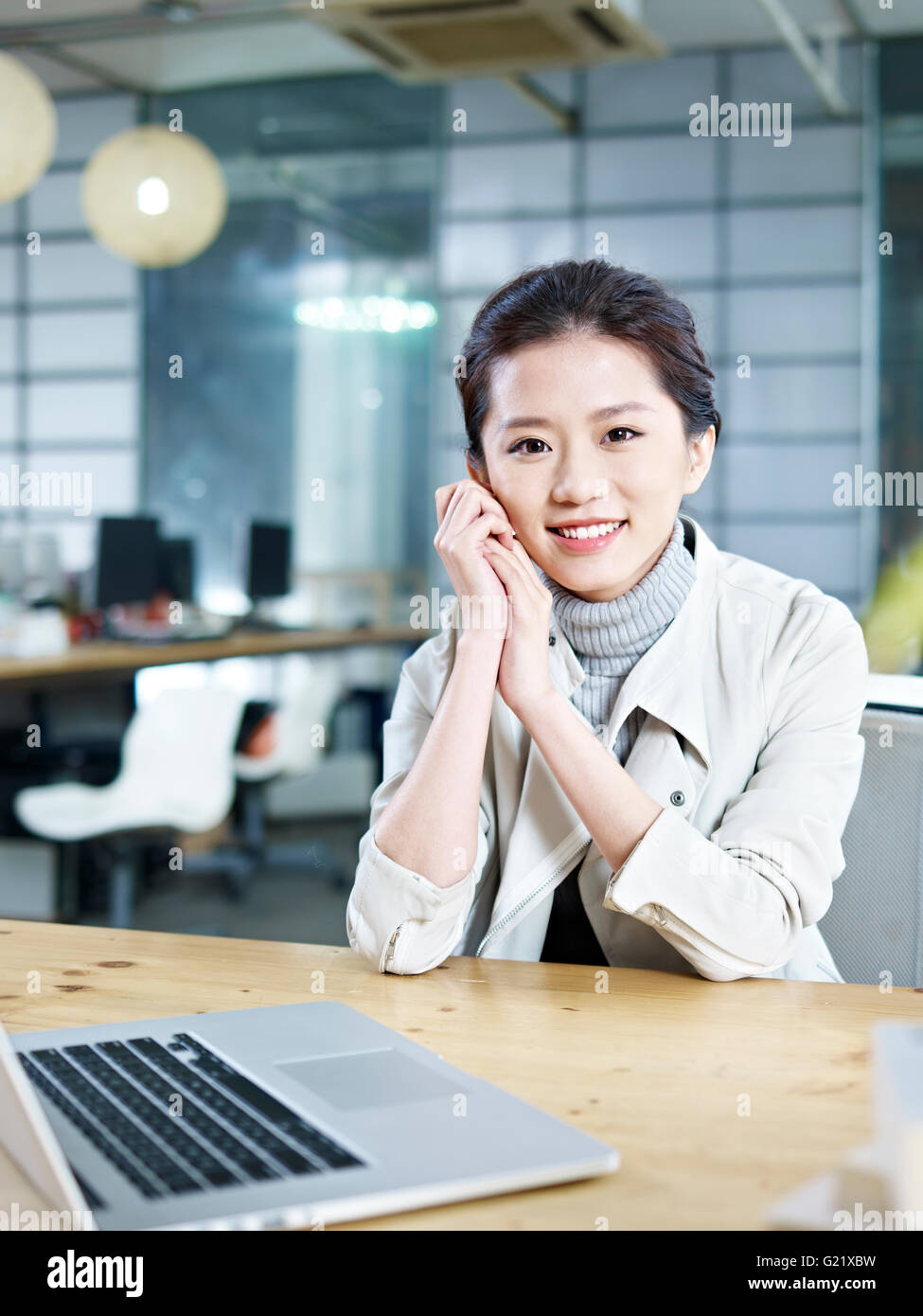 Young Asian businesswoman sitting at desk in office smiling at camera Banque D'Images