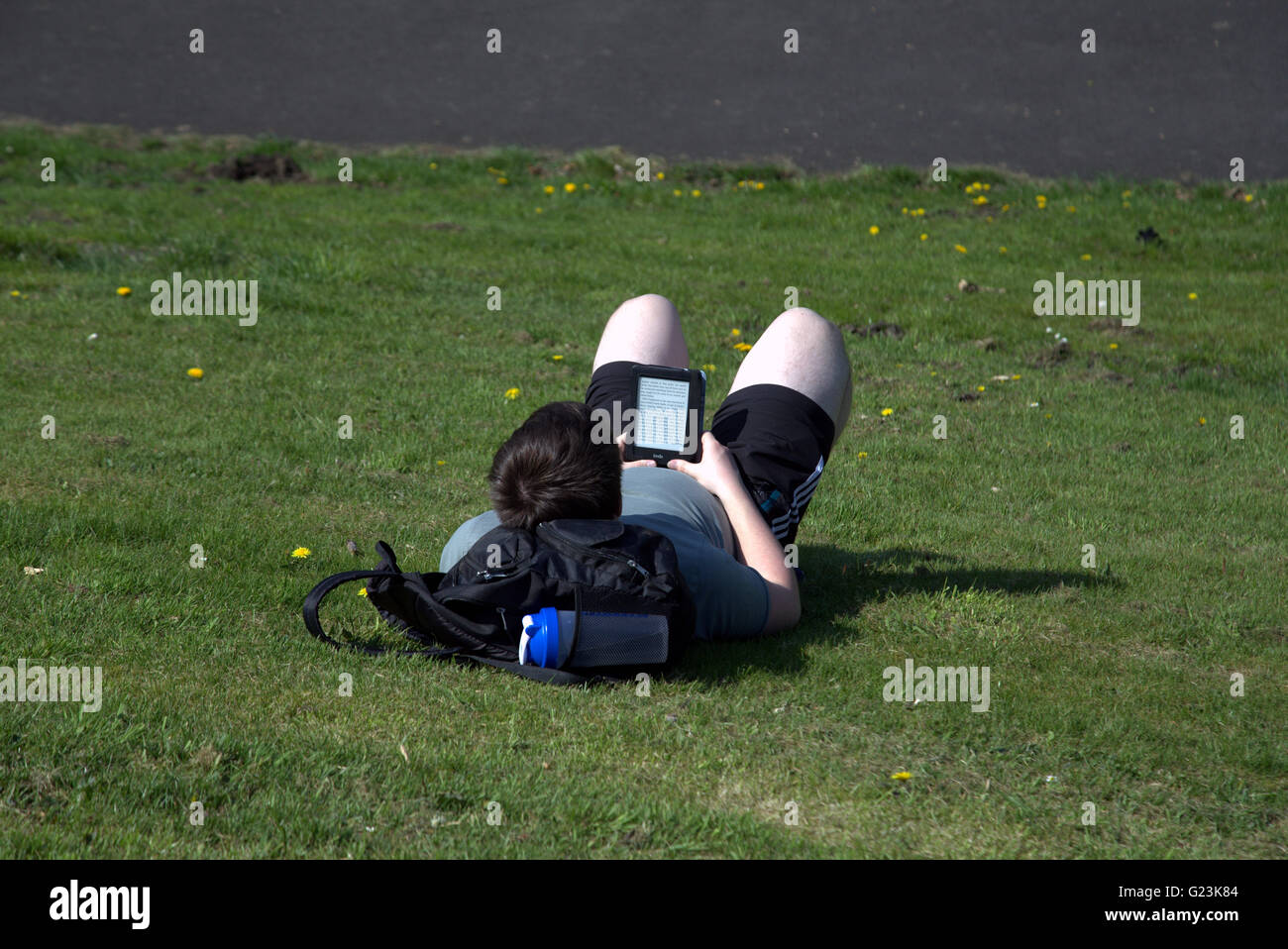 Homme ou garçon couché sur l'herbe lecture livre Kindle Reader dans le parc Kelvingrove Glasgow, Écosse, Royaume-Uni. Banque D'Images