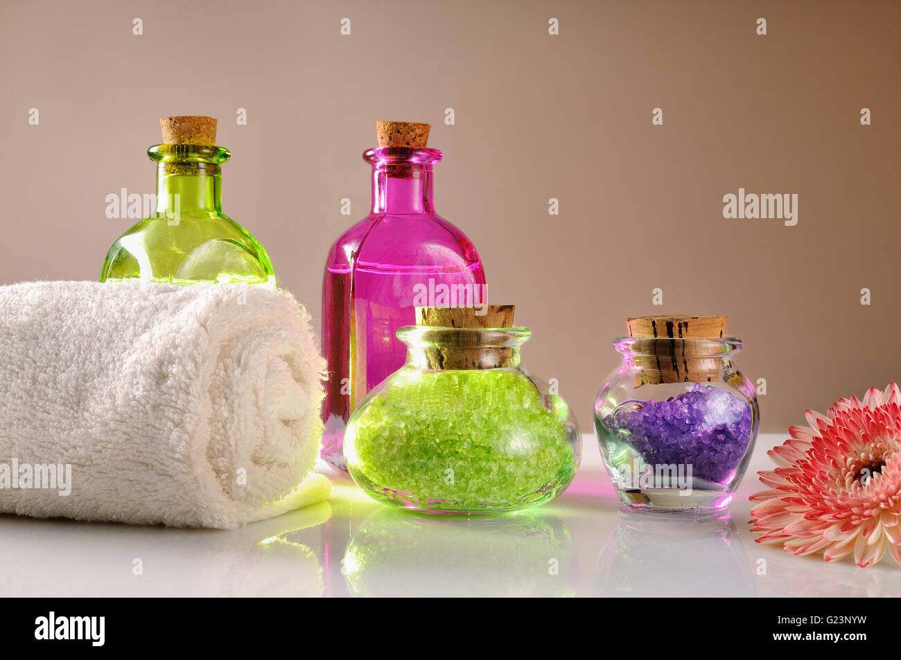 Huiles et Sels de bain sur table en verre blanc. Décoré avec fleur et serviette avec brown gradient background. Composition horizontale Banque D'Images