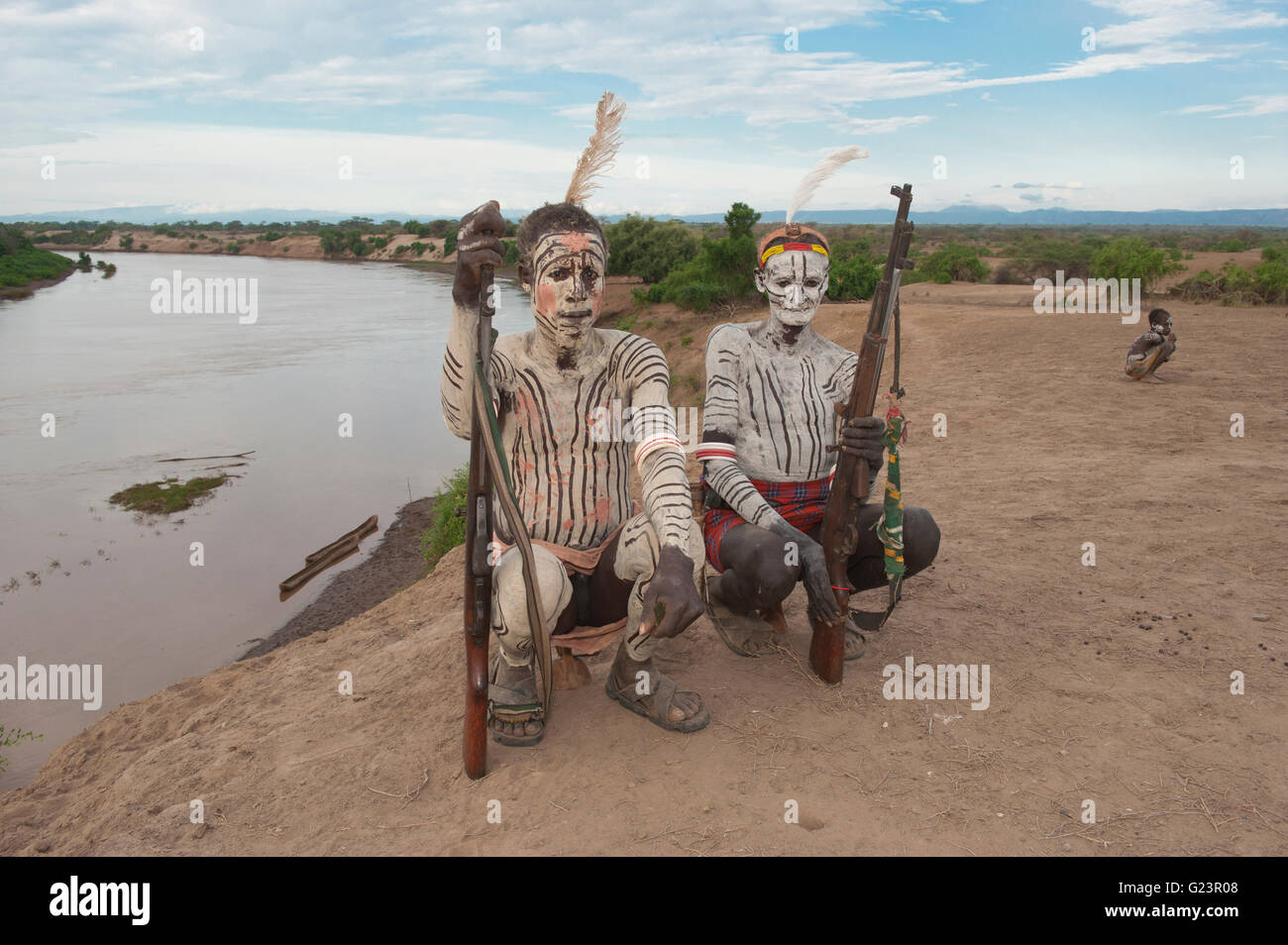 Deux guerriers Karo avec peintures du corps et du visage et au fusil assis sur leurs appui-tête, la vallée de la rivière Omo, dans le sud de l'Éthiopie Banque D'Images