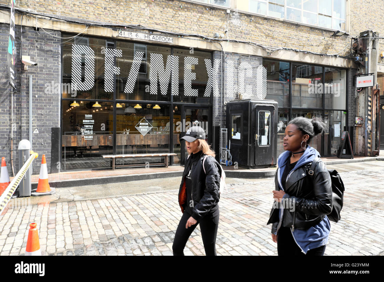 Les jeunes femmes marchant passé DF/Mexique Mexican Restaurant sur Dray à pied et Hanbury Street près de Brick Lane dans l'Est de Londres UK KATHY DEWITT Banque D'Images