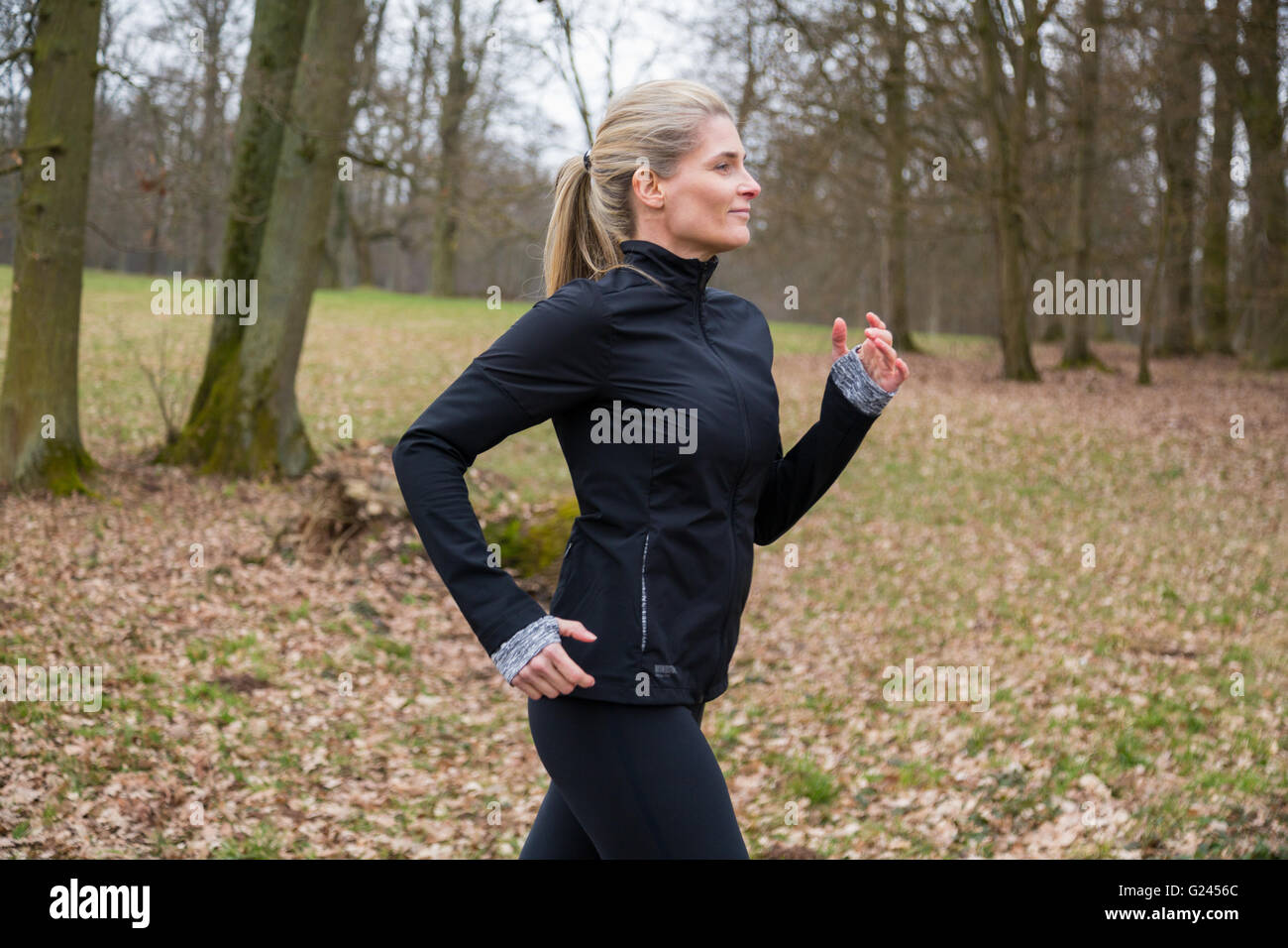 Femme d'âge moyen du jogging dans un parc en automne, derrière un fond de feuilles d'oranger. plan moyen. Banque D'Images