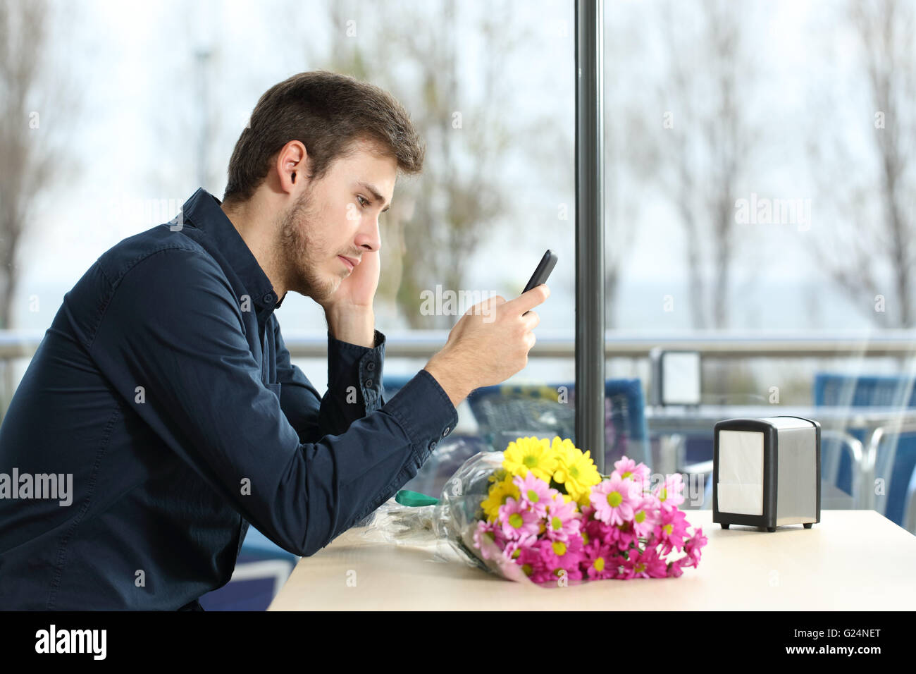 Homme triste avec un bouquet de fleurs a pris la parole à une date phone messages dans un café Banque D'Images