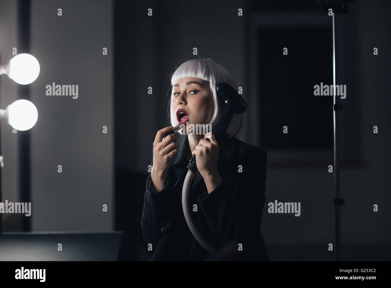 Bizarre belle jeune femme tenant défroisseur et appliquer le rouge à lèvres en dressing Banque D'Images