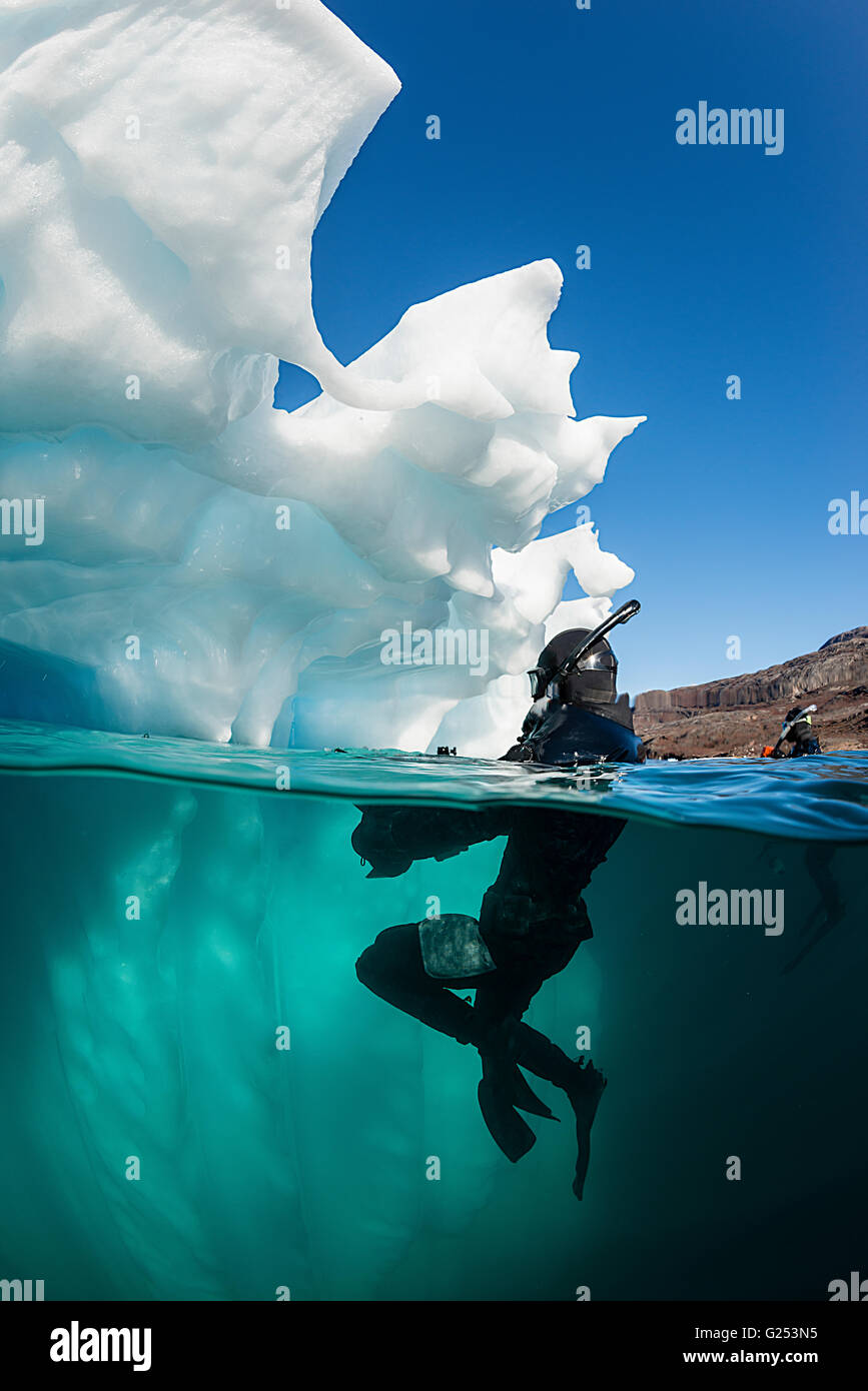 Plongeurs dans l'eau à côté d'un petit iceberg dans un fjord sur la côte est du Groenland. Banque D'Images