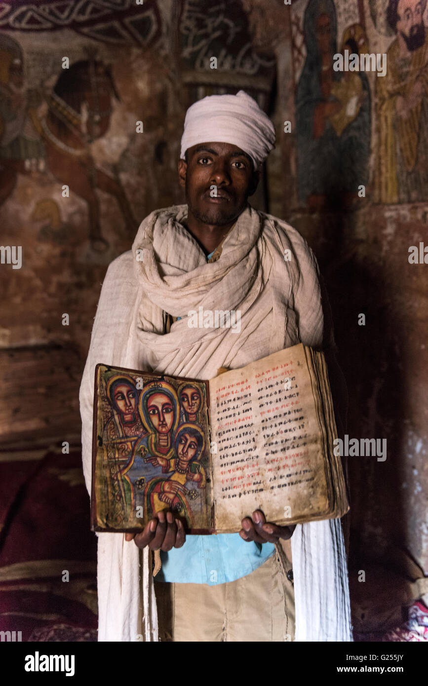 Prêtre orthodoxe holding saint livre à l'intérieur de l'église de roche taillé, Gheralta Ethiopie Banque D'Images