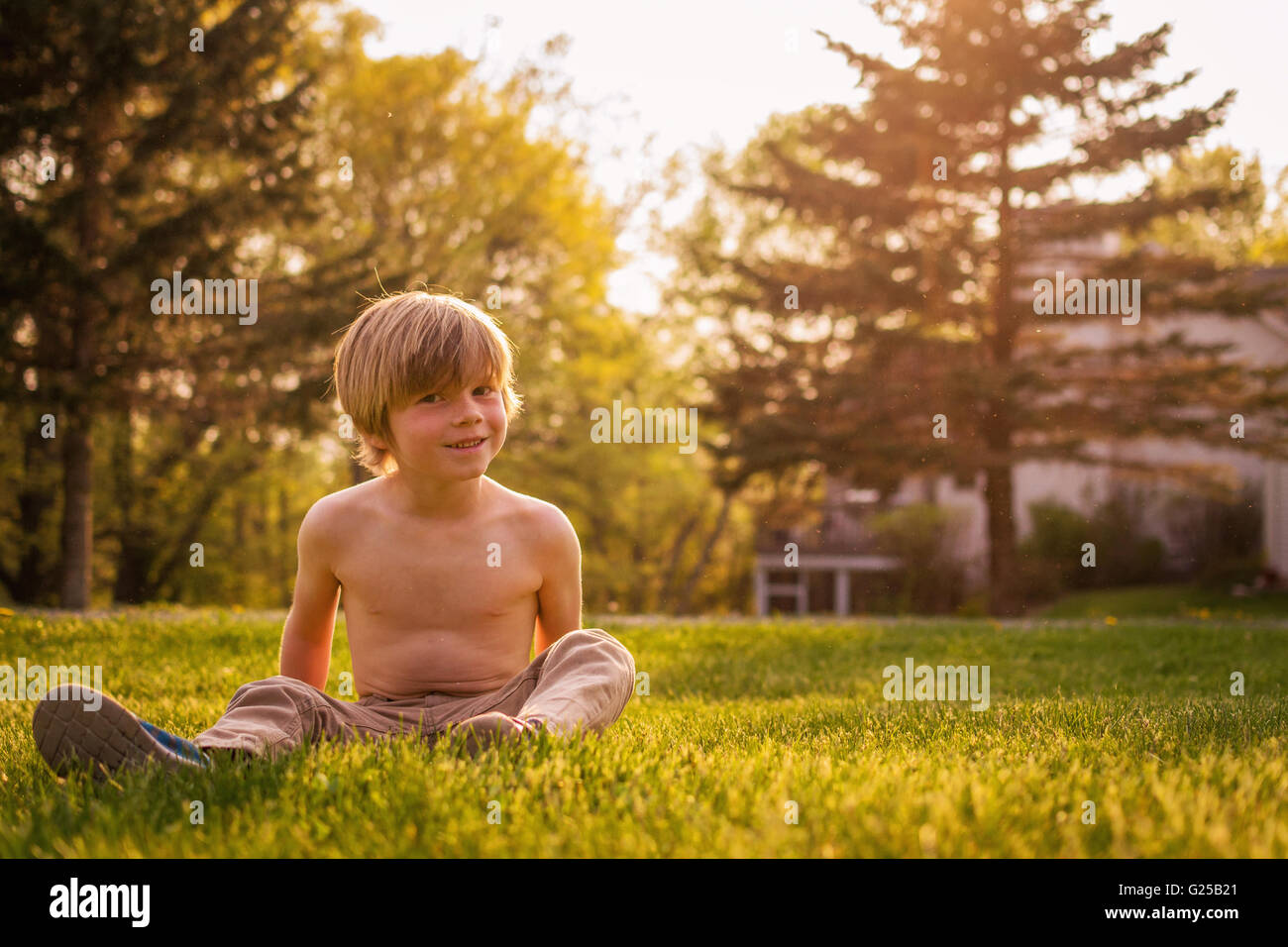 Garçon assis dans un jardin à l'herbe Banque D'Images