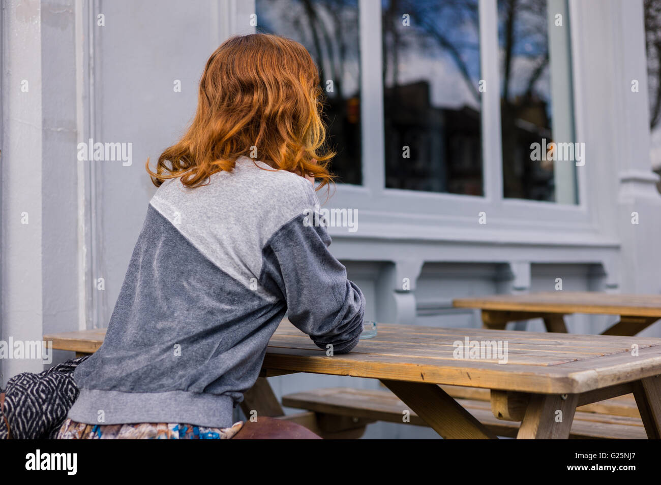 Une jeune femme est assise sur un banc à l'extérieur d'un pub ou restaurant sur un jour de printemps Banque D'Images