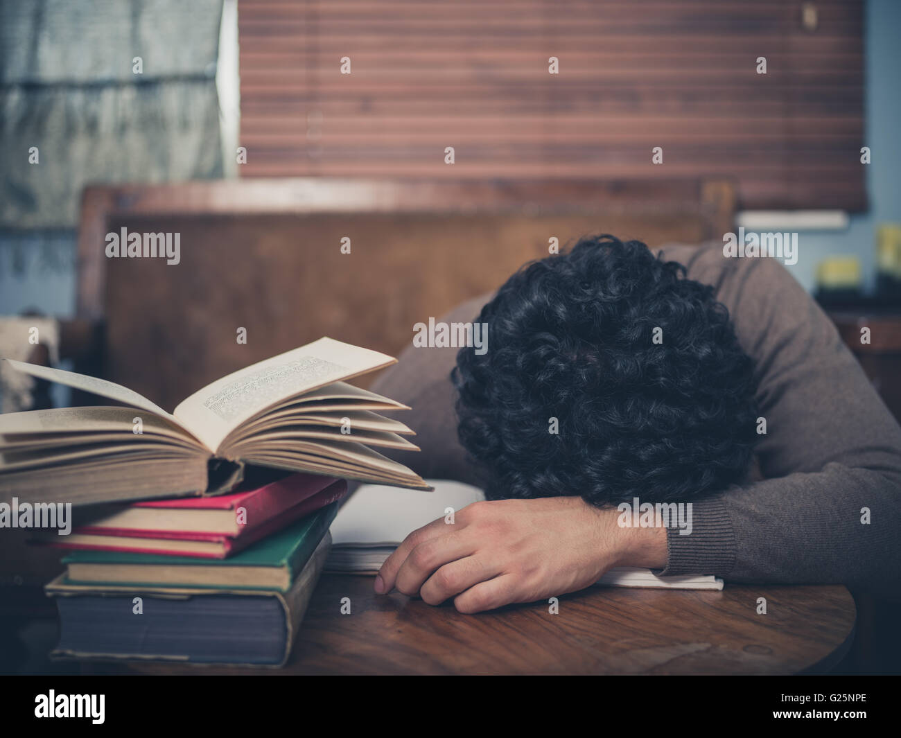 Un étudiant fatigué s'est endormi, la tête sur une table basse entourée de livres Banque D'Images