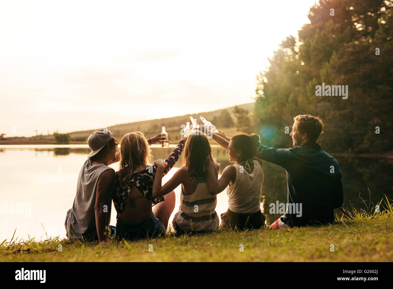 Groupe de jeunes gens assis dans une rangée à un lac avec des bières. Young Friends toasting et célébrer avec bières au lac sur une Banque D'Images