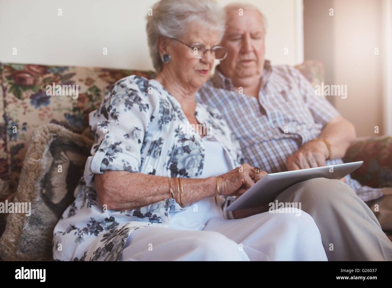 Portrait de vieille femme assise avec son mari et à l'aide de tablette numérique. Senior couple sitting on sofa at home avec une touche scre Banque D'Images