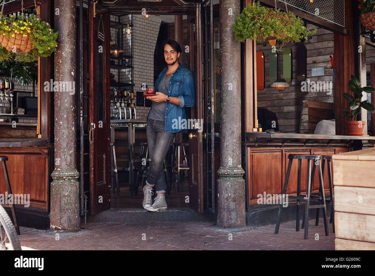 Portrait de l'atmosphère jeune homme debout à l'entrée d'un café et un café. Jeune homme élégant au café un ent Banque D'Images