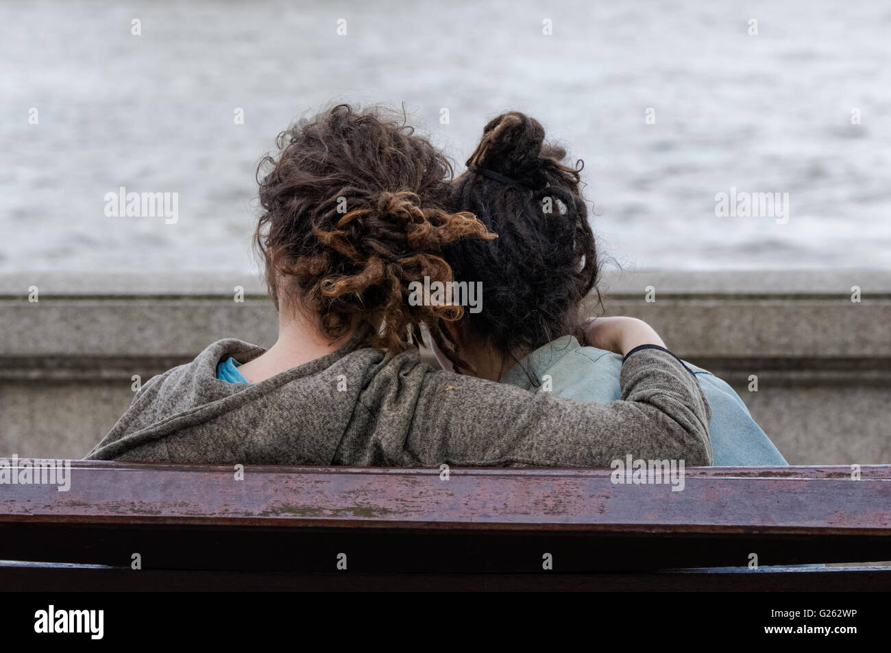 Jeune couple assis sur un banc sur la rive de la rivière, Londres Angleterre Royaume-Uni Banque D'Images