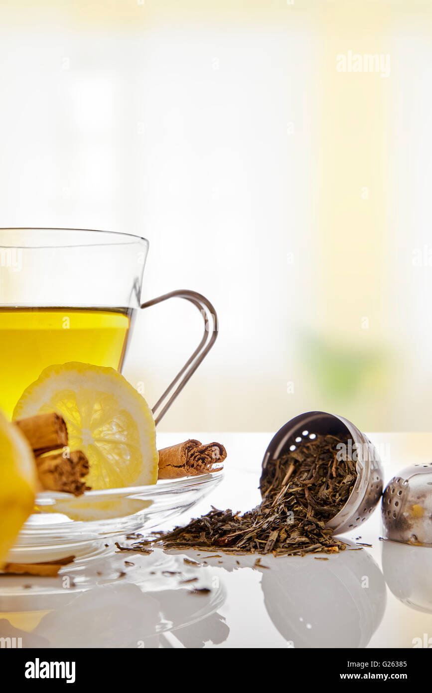 Tasse en verre de thé vert avec le bâton de cannelle et de citron sur une table dans le salon. Avec crépine métallique close up. Com horizontale Banque D'Images