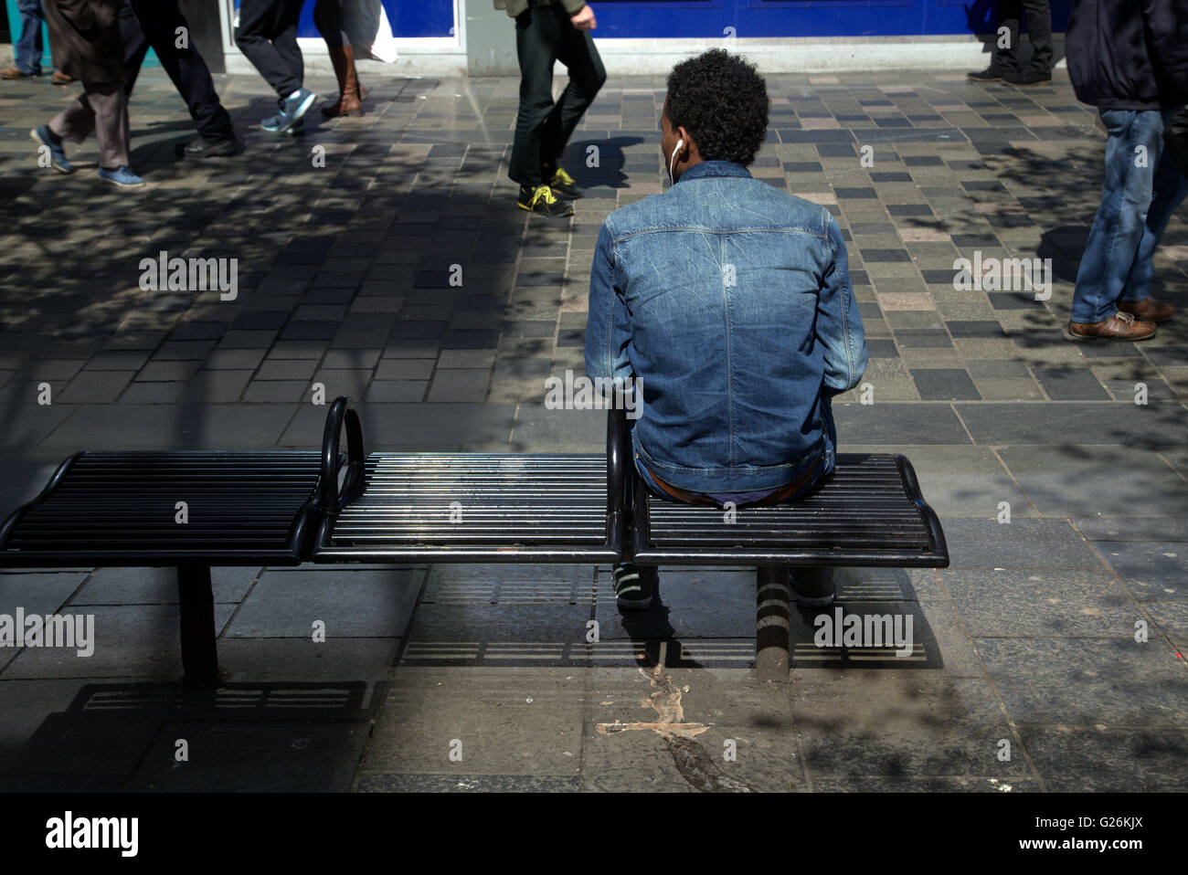 Jeune homme africain assis sur un banc avec écouteurs Glasgow, Écosse, Royaume-Uni. Banque D'Images