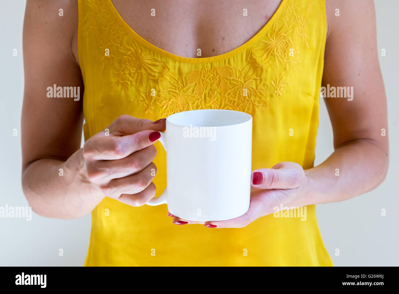 Main tenant une tasse de café blanc fond jaune d'or. Des maquettes, parfait pour mettre votre conception. Banque D'Images