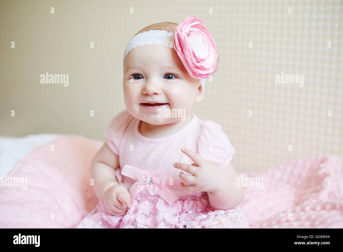 Cute magnifique petite fille assise sur un lit dans une robe rose et souriant Banque D'Images