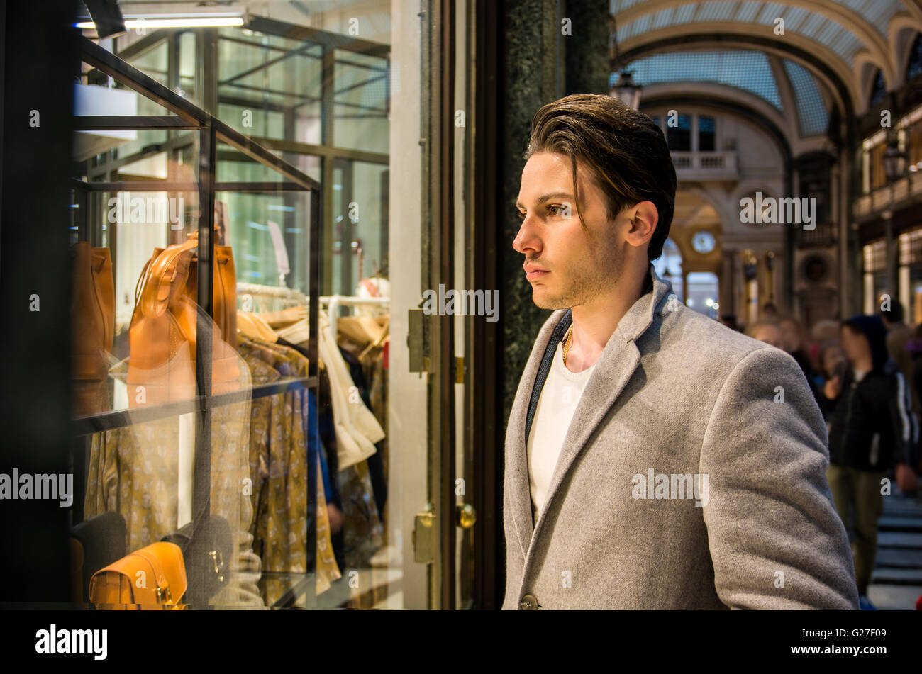 Beau Jeune homme en costume noir élégant à la recherche à l'Affiche d'articles de mode en verre Fenêtre Boutique au côté de la rue Haute. Banque D'Images