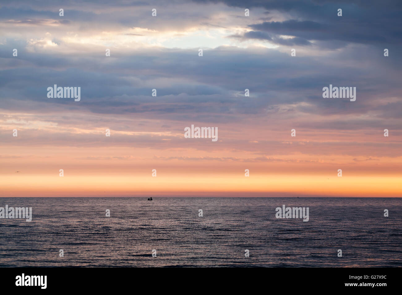 De soleil colorés sur la mer Baltique, ciel nuageux, encore de l'eau et les pêcheurs sur un petit bateau dans la distance Banque D'Images