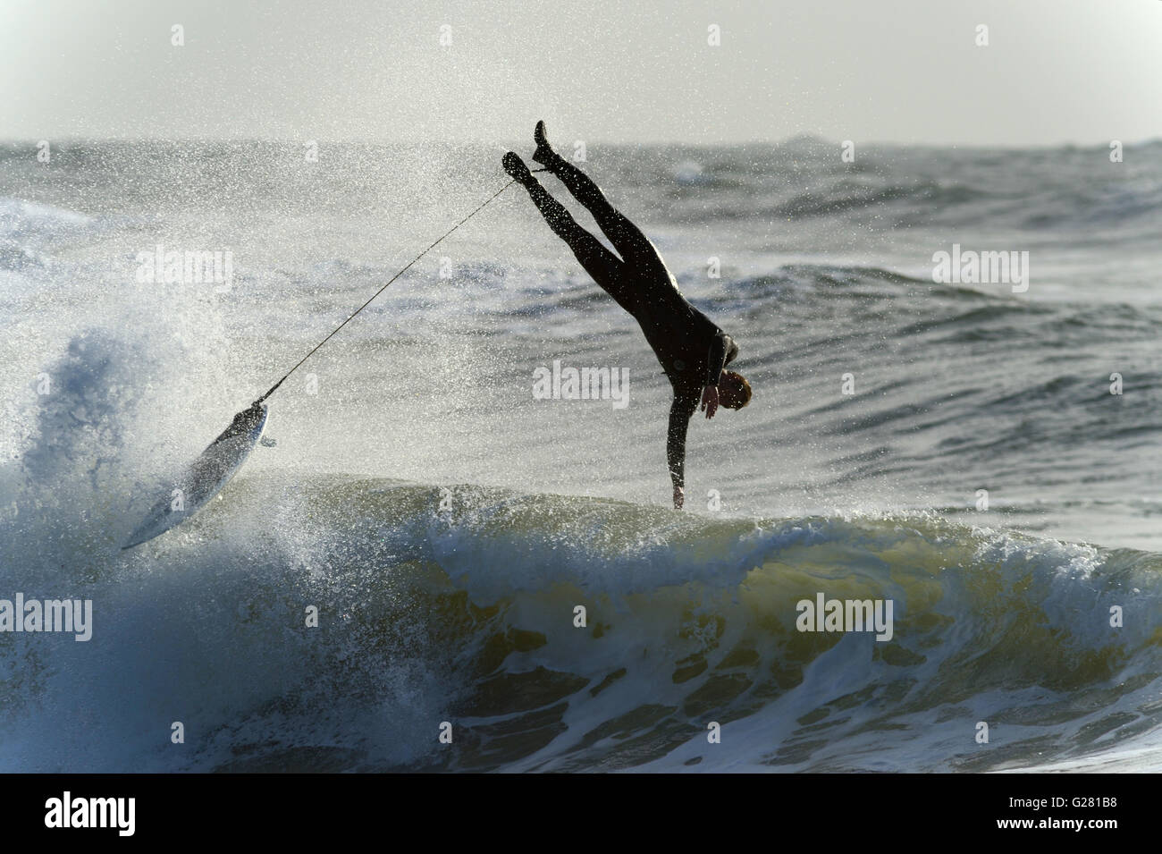 Attaché à son bord, un surfeur sur Gower dives sur le dos d'une vague dans un élégant wipe out. Le surf est très populaire au pays de Galles. Banque D'Images