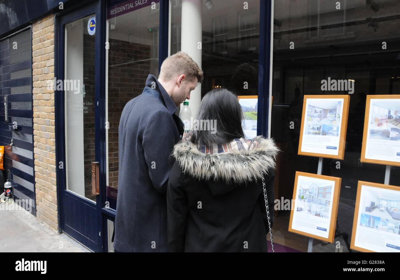 Un jeune couple qui regarde le prix de l'immobilier, dans une fenêtre de l'agent immobilier , dans Brick Lane, East London Banque D'Images