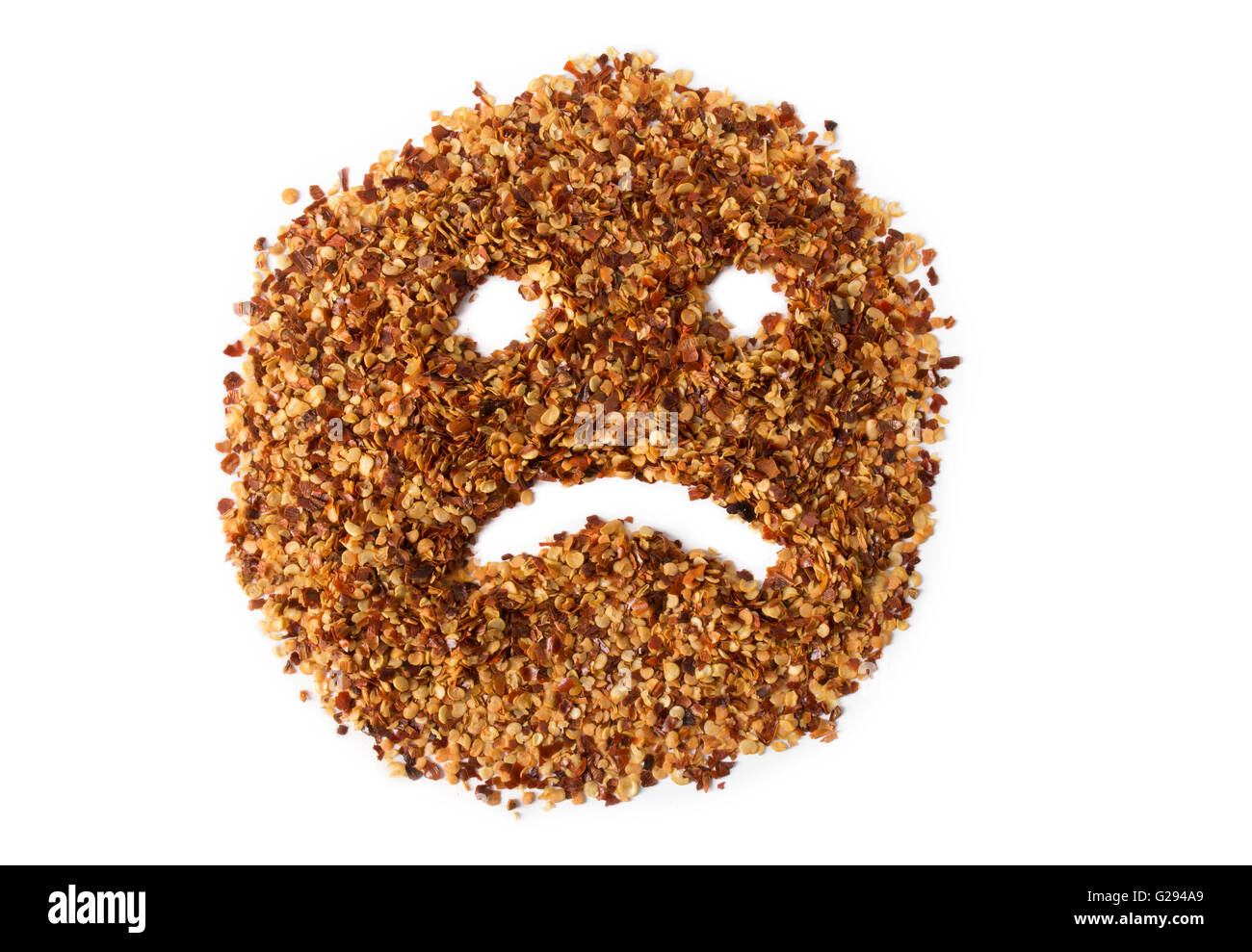 Un tas de flocons de piment rouge broyé montrant un visage triste, représentant d'estomac ou l'indigestion. Banque D'Images
