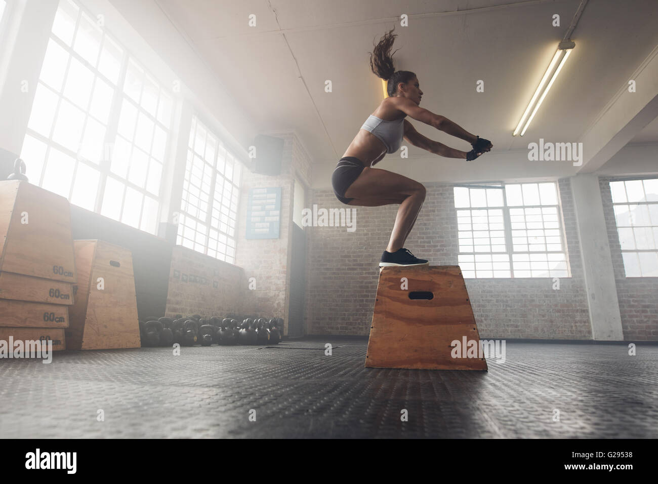 Vue côté droit de monter jeune femme faisant un saut de l'exercice. La femme d'un squat à la croix de mettre en place une salle de sport Banque D'Images