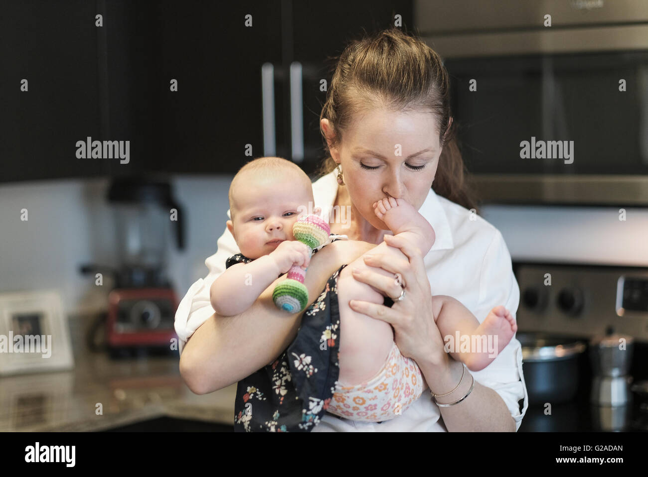 Mère embrassant bébé fille (2-5 mois) pieds Banque D'Images
