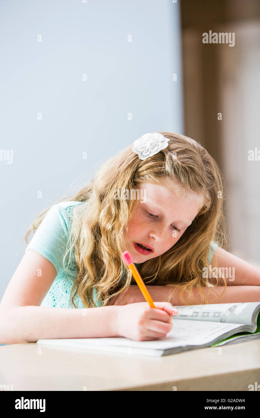 Blonde girl (8-9) doing homework at table Banque D'Images