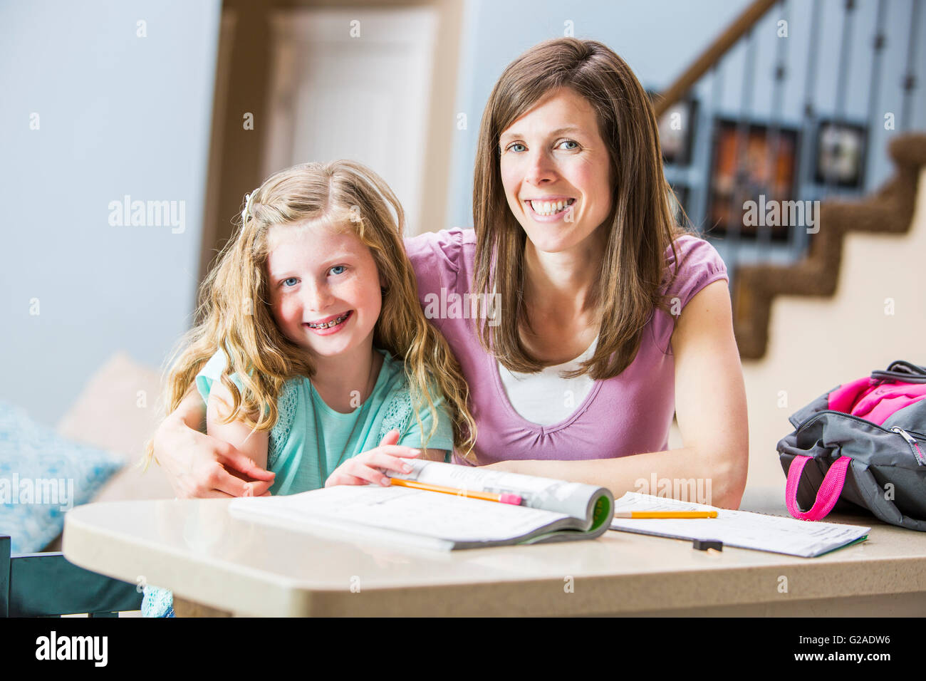 Smiling mother and daughter (8-9) sitting at table étudiant Banque D'Images